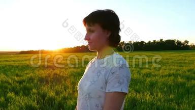 一个年轻女子站在一片绿色的草坪上，在日落的背景下缓慢的动作
